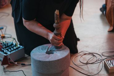 Person holding a wooden tool on a stone mill surrounded by electronic equipment.