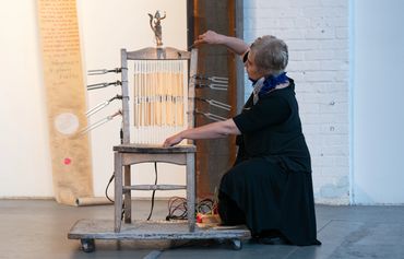 A woman interacts with a wooden chair modified with tuning forks and wires.