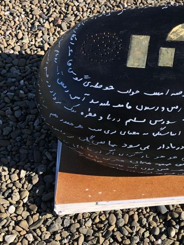 Oval-shaped black object with golden geometric shapes and white script, placed on a notebook on gravel.
