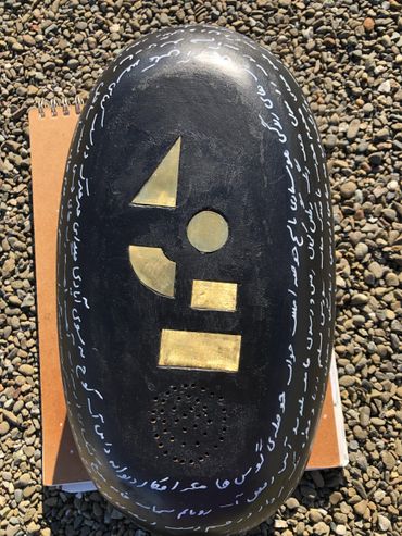 Black oval object with golden geometric shapes and white script on its edges.
