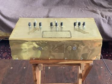 Custom-made brass electronic device with knobs and switches on a wooden stand.