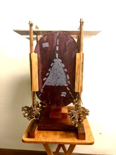 Abstract wooden sculpture with a painted oval centerpiece on a small table.
