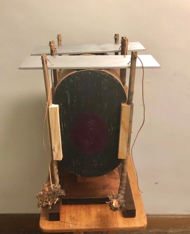 Handmade wooden contraption with a central black circular board and natural materials.
