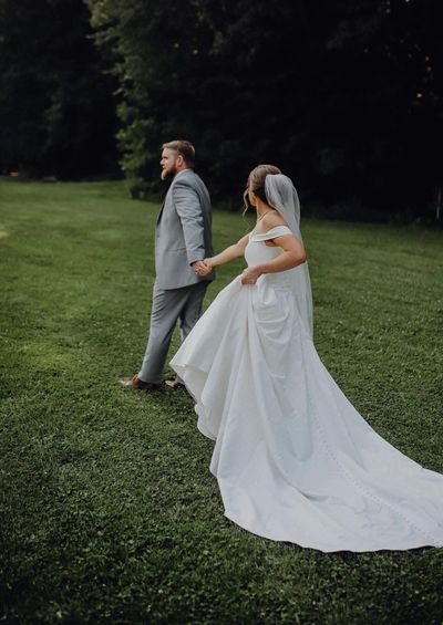 Bride and groom holding hands, walking on green grass outdoors.