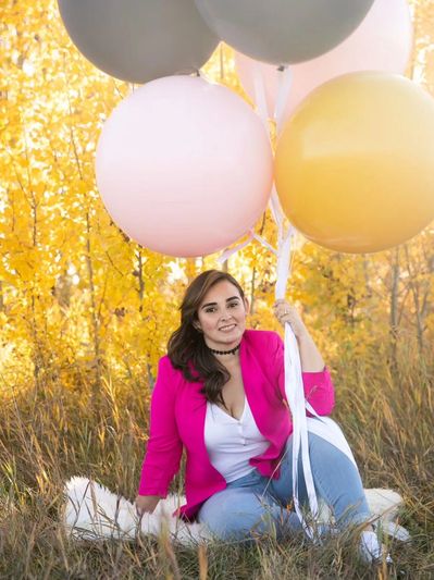 Carolina sits in the grass, holding a bunch of helium jumbo balloons.