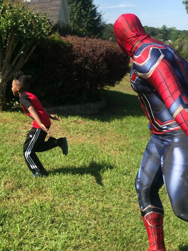 Child running away from a person dressed as Spider-Man in a yard.