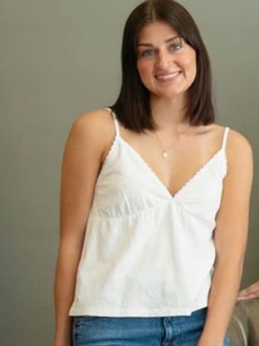 A young woman smiling, wearing a white sleeveless top and blue jeans.