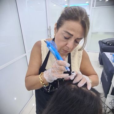 A woman performing a procedure with a blue device on another person's hair.