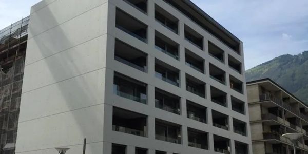Edifico moderno con balconi e montagna sullo sfondo.