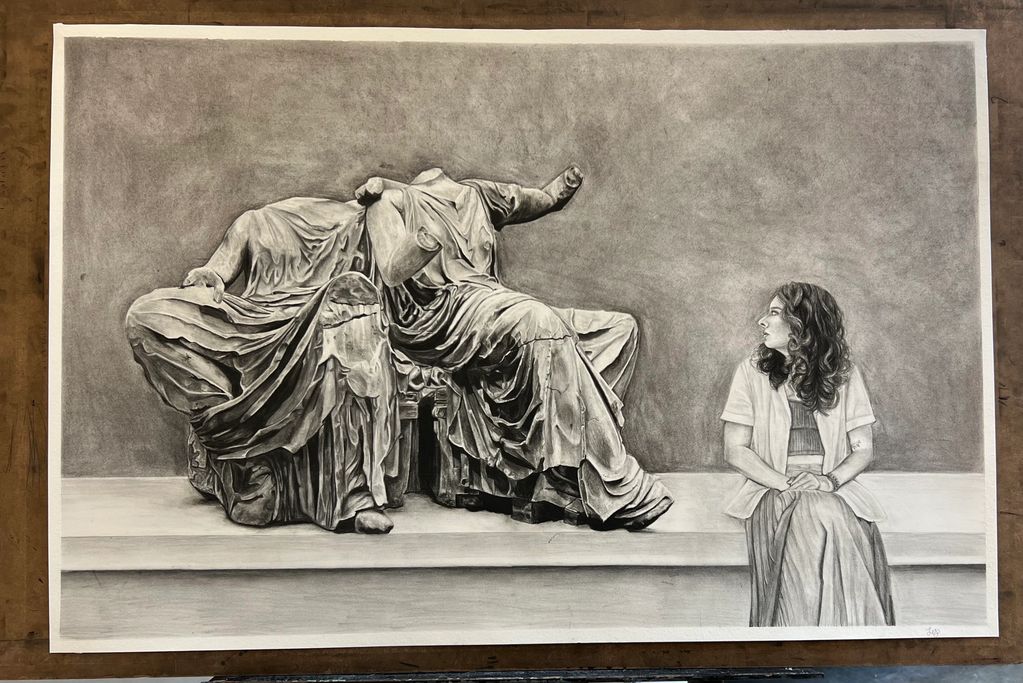 A woman sitting beside two ancient headless statues, both looking towards each other.