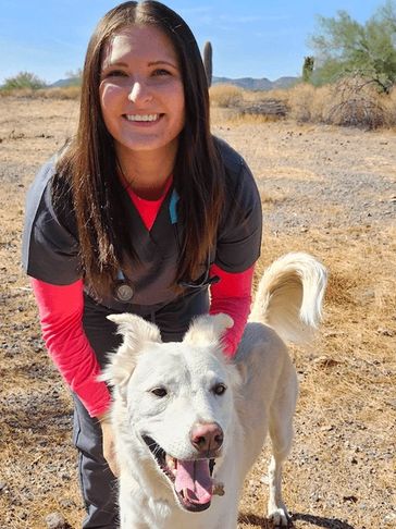 Jessica smiling in scrubs with a happy white dog outdoors.