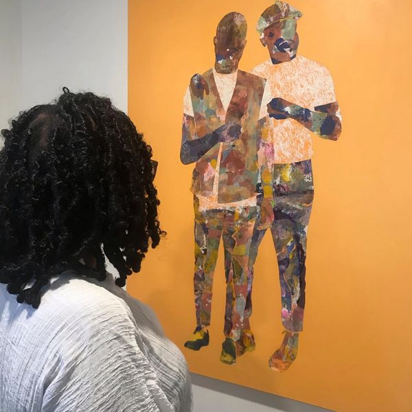 Person observing a colorful abstract painting of two figures on an orange background.