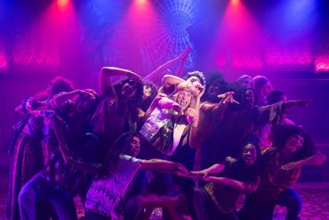 A lively group of people posing energetically with colorful stage lighting.