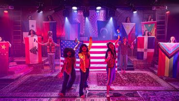 Performers on stage holding various national flags under colorful lights.