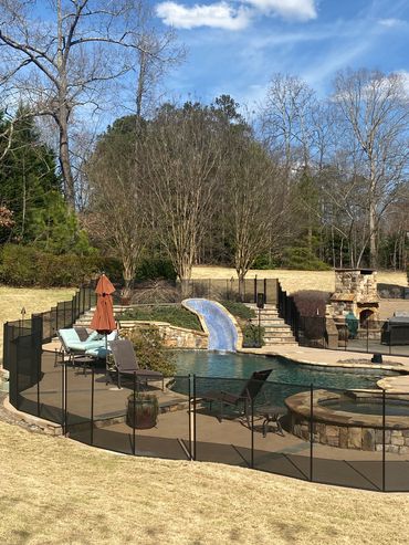 Outdoor pool area with lounge chairs, slide, and stone fireplace under blue sky.