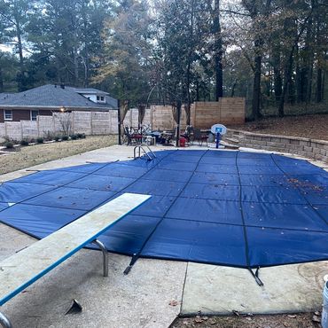 Backyard pool covered with a blue safety cover and a diving board.