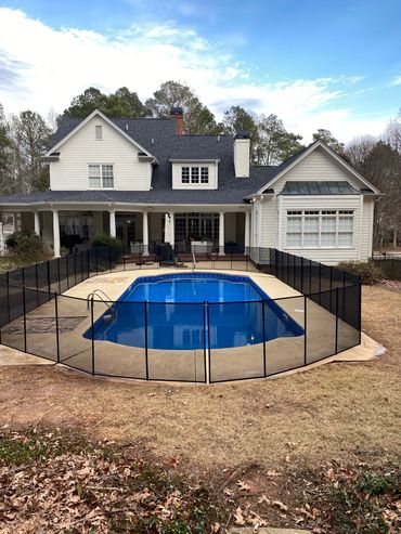 A backyard pool surrounded by a safety fence in front of a large house.