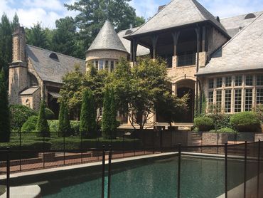 Elegant brick house with a fenced swimming pool and lush greenery.