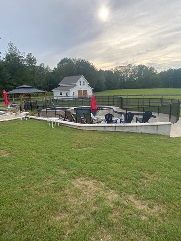Outdoor pool area with chairs, umbrellas, and a white barn in the background.