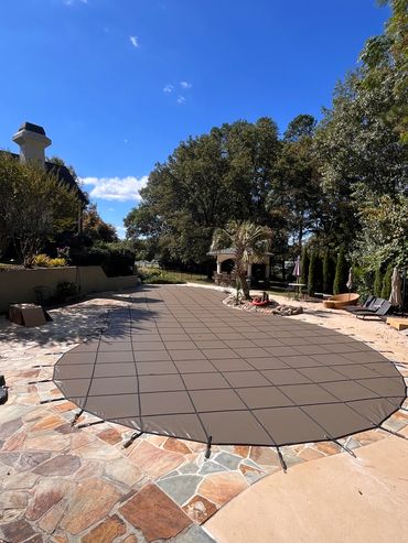 A covered swimming pool in a sunny backyard with stone and concrete surroundings.