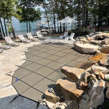 Covered pool in a scenic backyard with lounge chairs and a lake view.