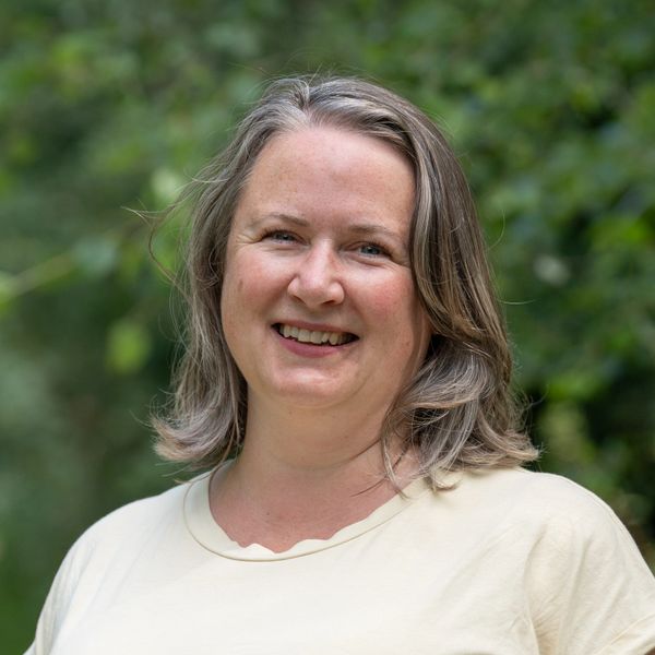 Friendly, smiling woman in front of soft, leafy green background.