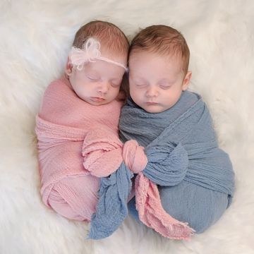 Two newborn babies swaddled and sleeping, holding hands.