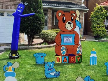 A teddy bear new baby yard sign with assorted baby lawn decorations and a blue air dancer