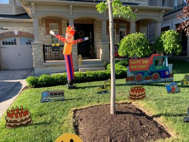 A birthday party clown inflatable wind dancer beside a birthday lawn card and assorted lawn ornament