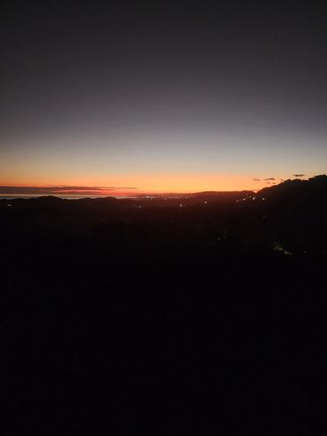 A serene sunset with a gradient sky over silhouetted hills and distant city lights.