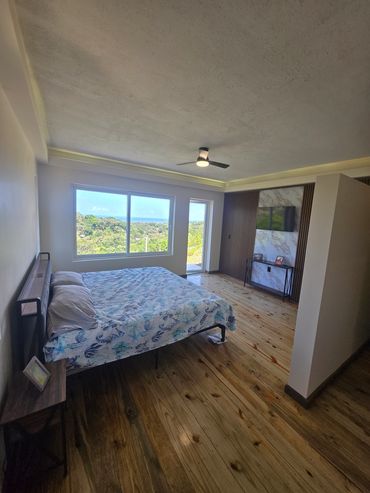 Modern bedroom with wooden floor and large window overlooking greenery.
