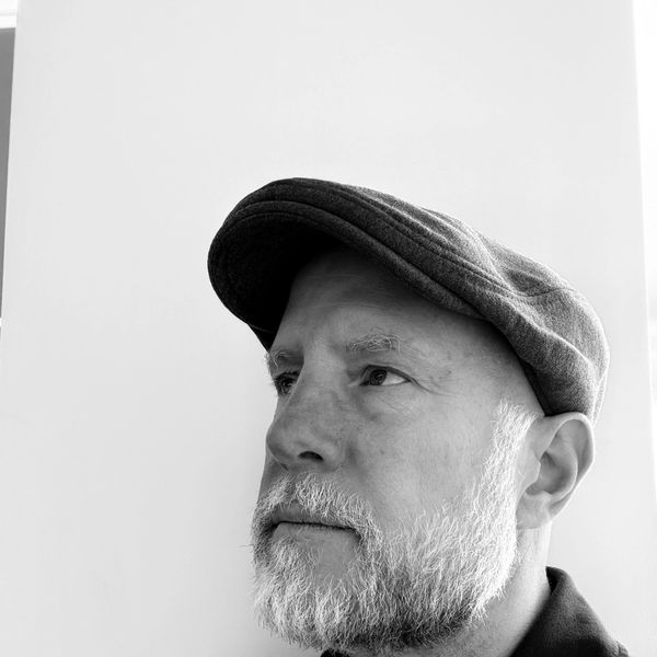 Black and white portrait of a man with a beard wearing a flat cap.