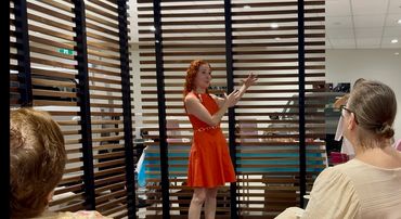 Leanne Zaccar wearing an orange dress giving a keynote at Mazda Brookvale