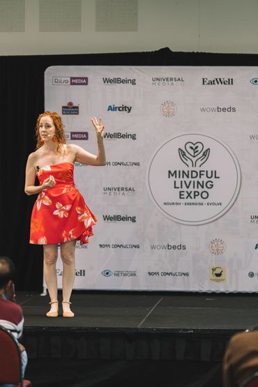 On am main stage at Mindful Living Expo, motivational keynote speaker, Leanne Zaccar wears a pink d