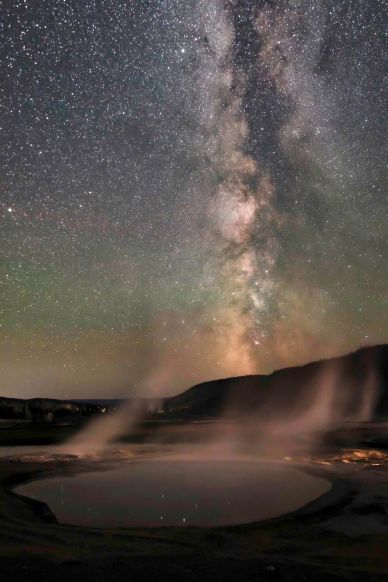 Milky Way over a steaming hot spring at night.