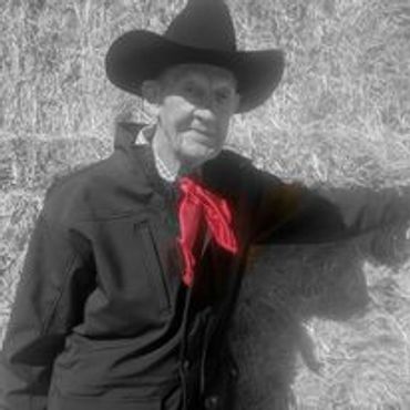 Elderly man in cowboy attire standing by hay bales.