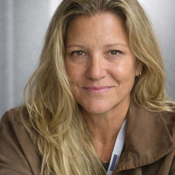 Smiling woman with long blonde hair and brown coat.