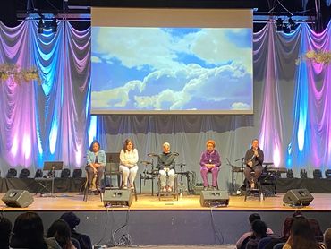 Panel discussion on stage with colorful lighting and cloud projection.