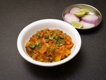 A bowl of mixed vegetable curry with a side of sliced onions and lime.