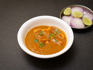 Spicy Indian curry served with sliced onions and lime wedges.