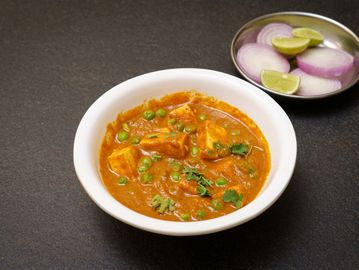A bowl of Indian curry with peas and paneer, served with sliced onions and lime.