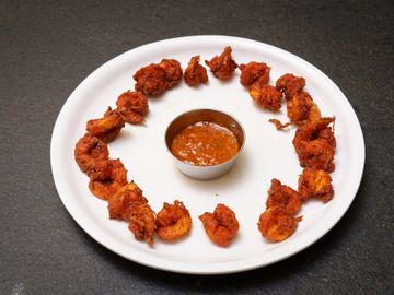 Plate of crispy fried shrimp with dipping sauce in the center.