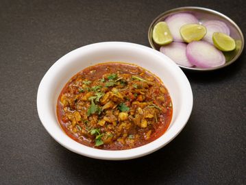 Bowl of spicy Indian curry with a side of sliced onions and lime.