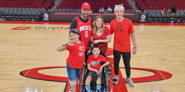 A family posing on the Houston Rockets basketball court, wearing team apparel.