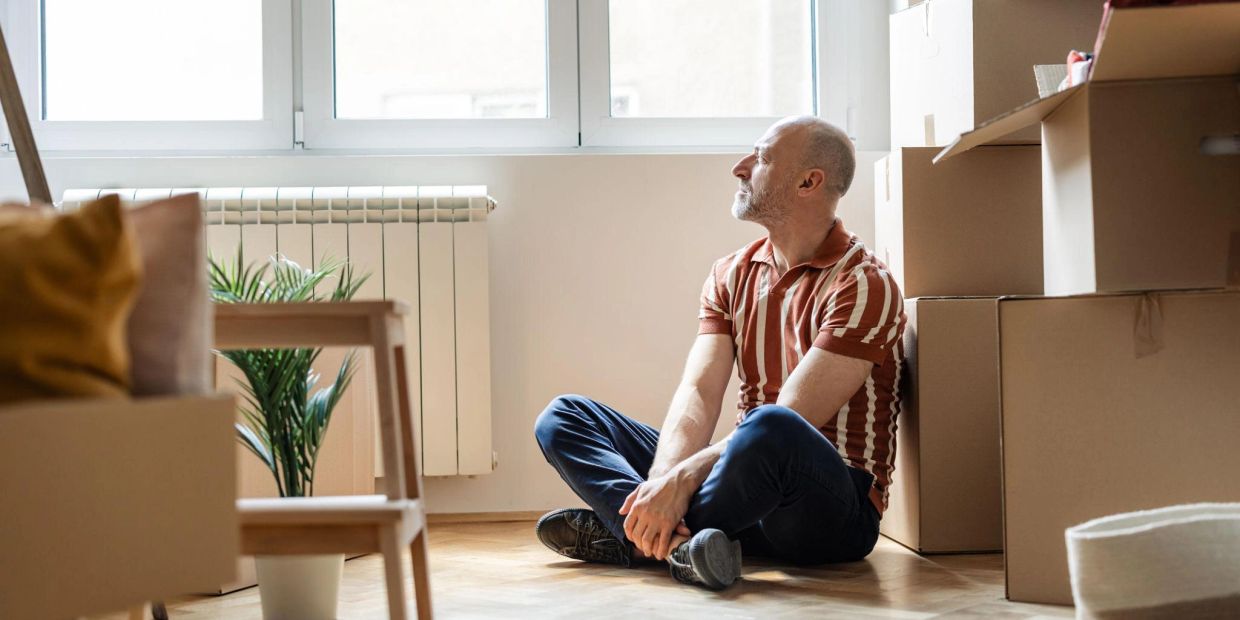 Man sitting in his empty home surrounded by boxes after a marriage breakdown