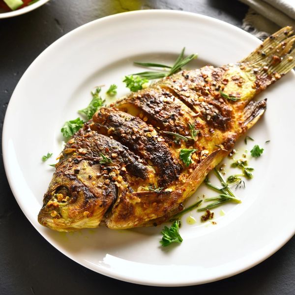 Grilled whole fish garnished with herbs and spices on a white plate.