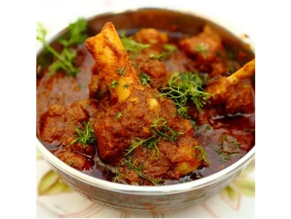 Spicy mutton curry garnished with fresh herbs in a bowl.