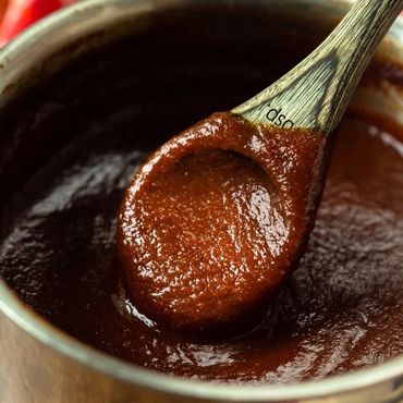 A wooden spoon scooping thick, rich barbecue sauce from a pot.