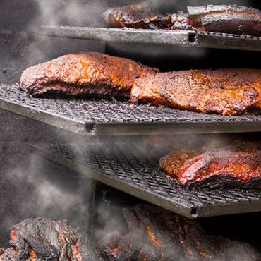 Smoky BBQ ribs cooking on multiple grill racks.