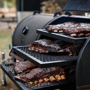 Smoked ribs cooking on a multi-level grill outdoors.